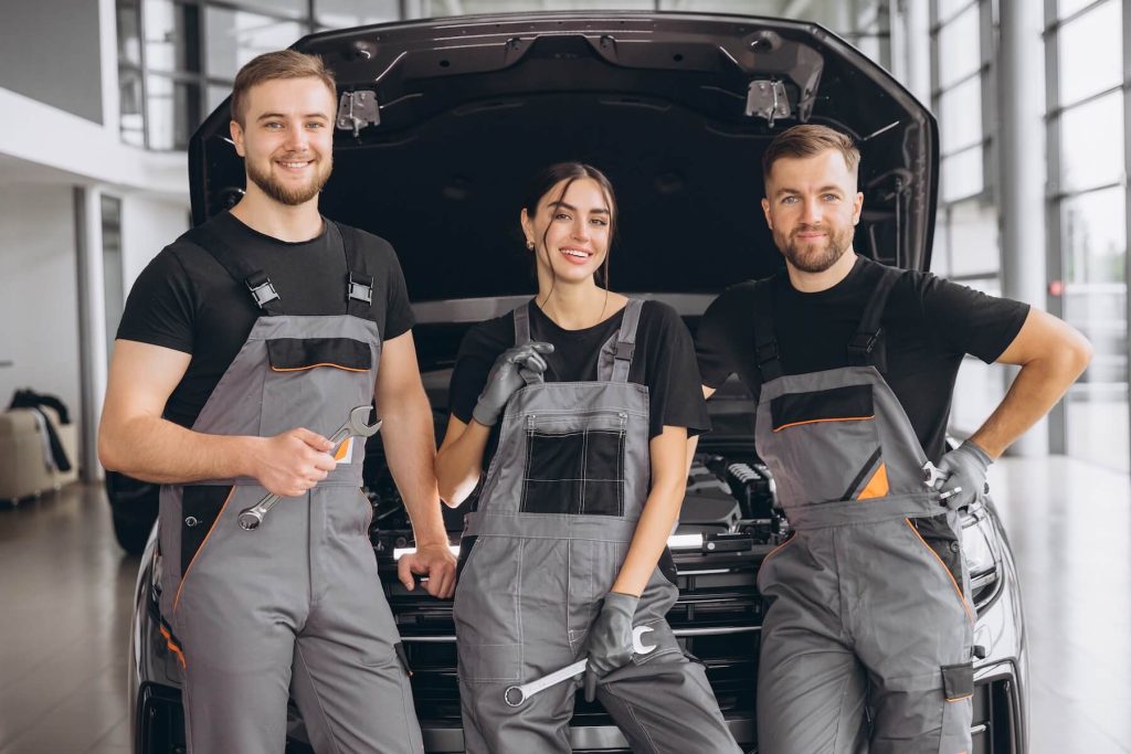 Three auto mechanics standing by open car hood